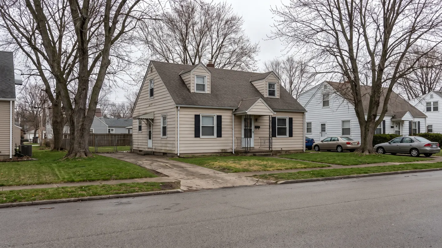 A post war Cape Cod house with dormer windows and pale siding on a flat street with bare winter trees, typical of everyday residential Dayton, Ohio