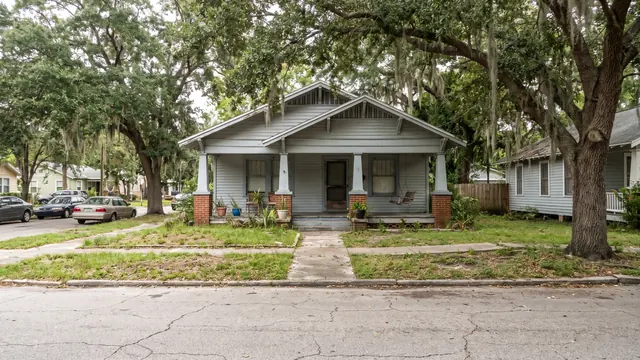 A 1920s craftsman bungalow with a deep front porch and tapered columns, shaded by a live oak, typical of the older residential neighbourhoods of Tampa, Florida